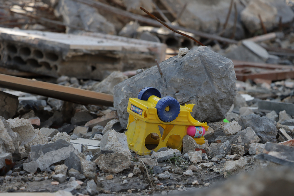 Yellow toy truck lies amidst rubble and debris, symbolizing destruction and abandonment in a chaotic, post-disaster urban environment. impact of disasters on everyday life, or the loss of innocence.